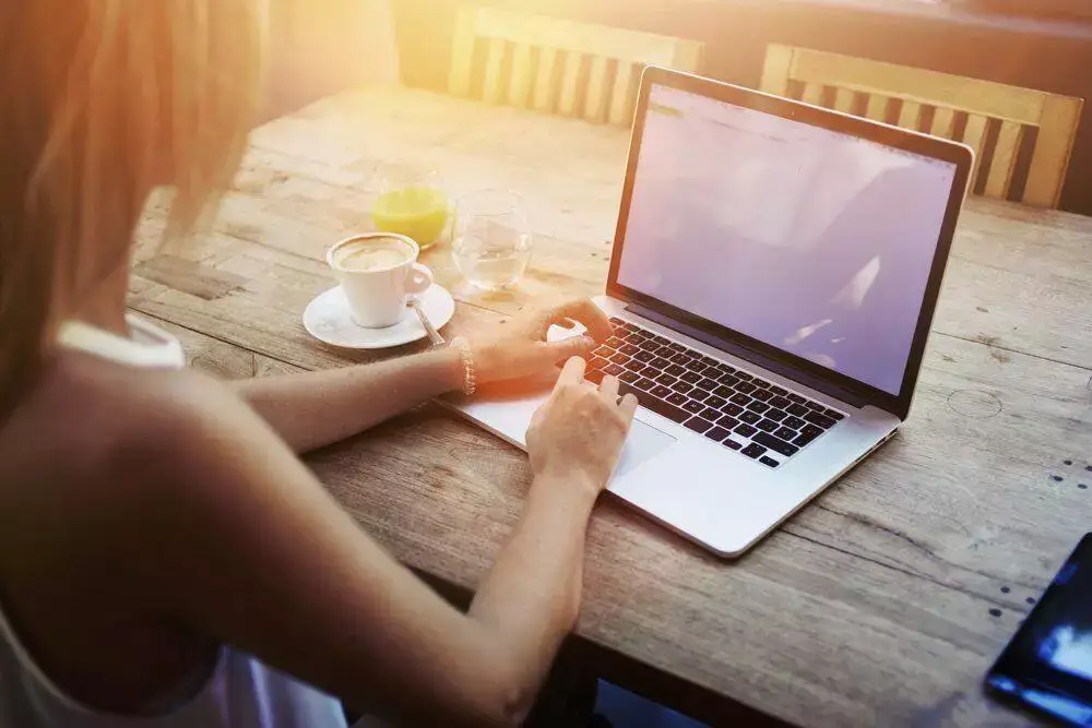 Cropped shot view of young woman keyboarding on laptop computer with blank copy space screen while sitting in cafe, blonde female student working on net-book after her lectures in University, flare sun.